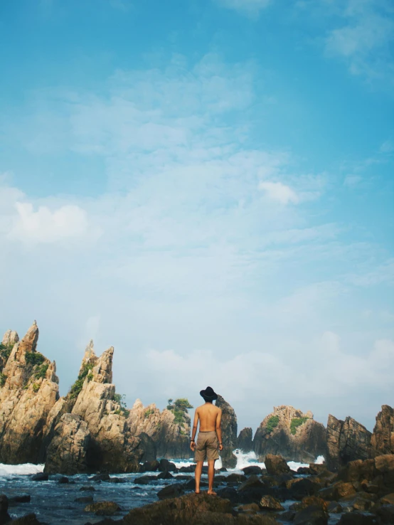 a man standing on top of a rocky beach, by Shen Quan, unsplash, process art, vietnam, tall stone spires, conde nast traveler photo, facing away