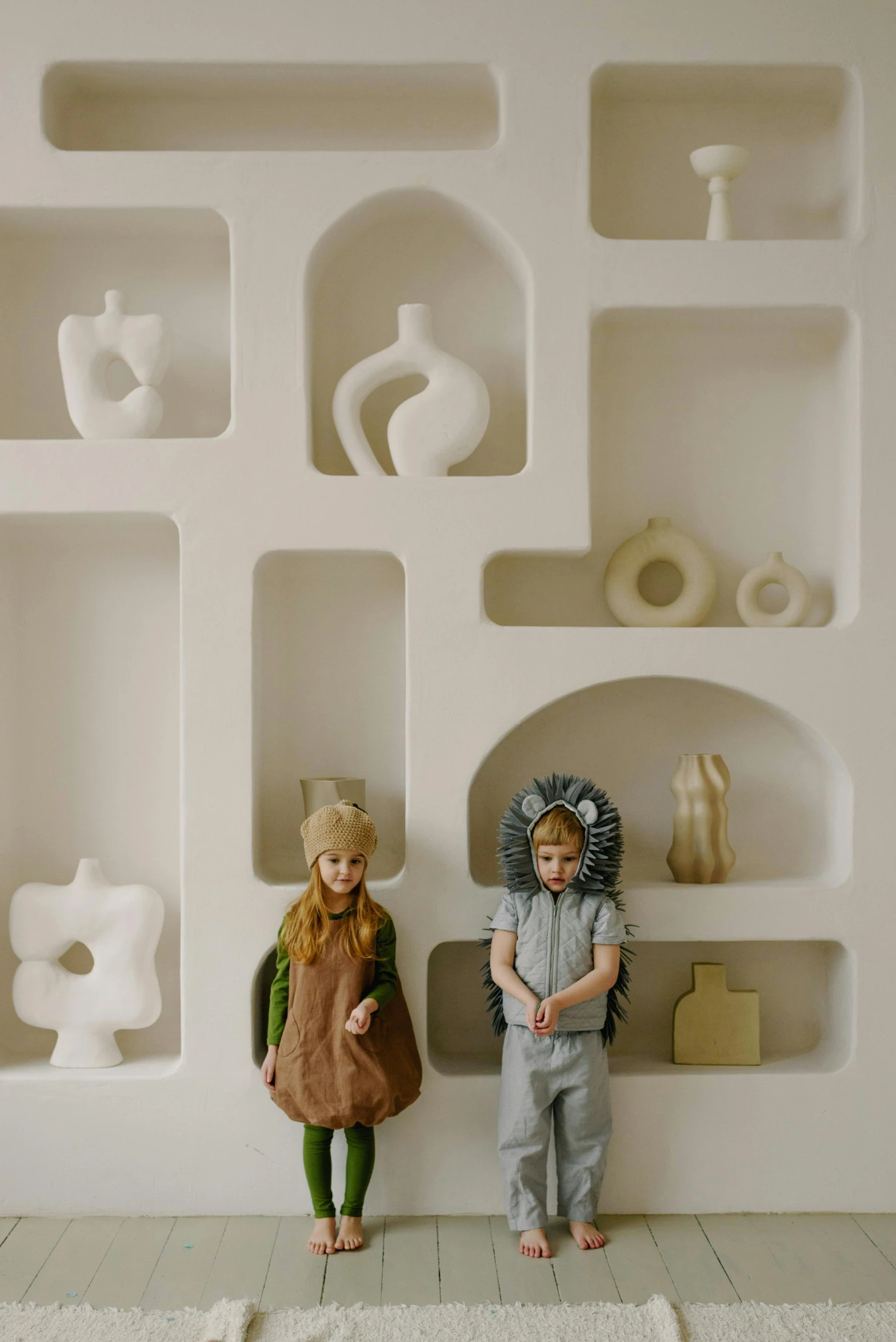 a couple of kids standing next to each other, a surrealist sculpture, inspired by Elsa Beskow, pinterest, conceptual art, 70s interior with arched windows, white ceramic shapes, softplay, flat lay