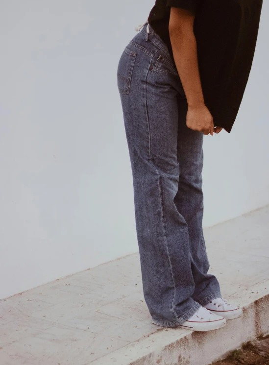 a woman standing on a ledge with her back to the camera, baggy jeans, right side profile, perfectly shaded body, flares