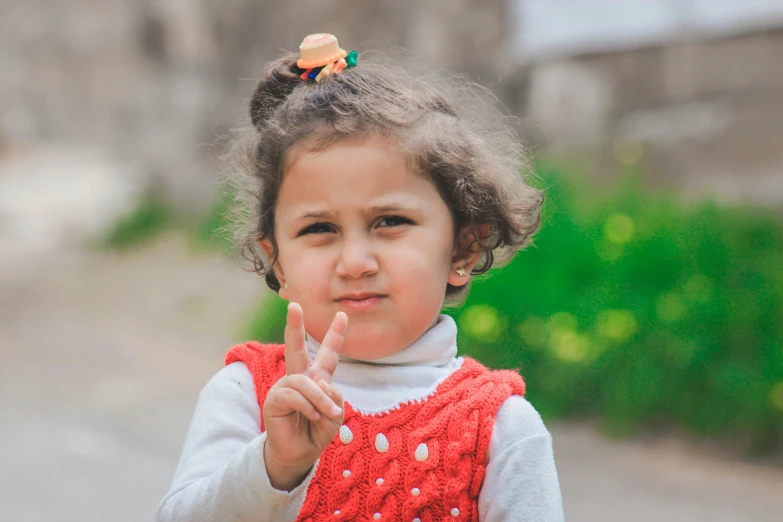 a little girl making a peace sign with her hand, pexels contest winner, wearing a red gilet, from egypt, 2 years old, serious face