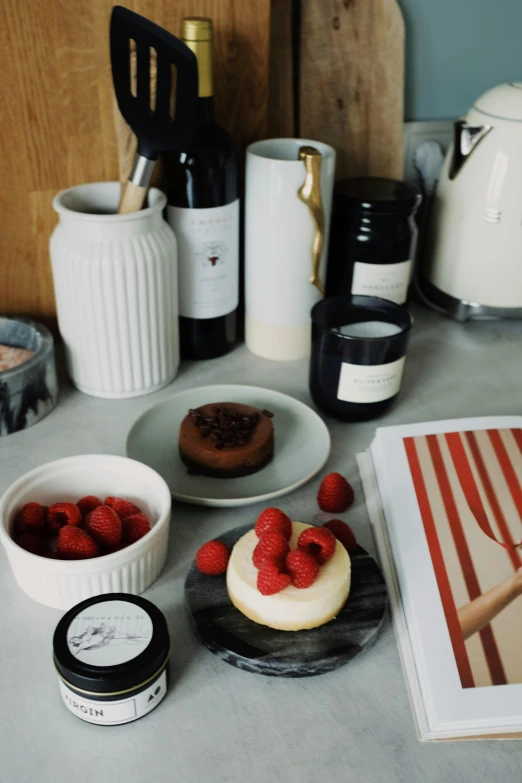 a book sitting on top of a counter next to a bowl of raspberries, a still life, unsplash, tins of food on the floor, cakes, red white and black, dwell