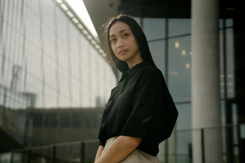 a woman standing in front of a building, inspired by Cheng Jiasui, pexels contest winner, realism, black shirt, looking towards camera, issey miyake, asher duran