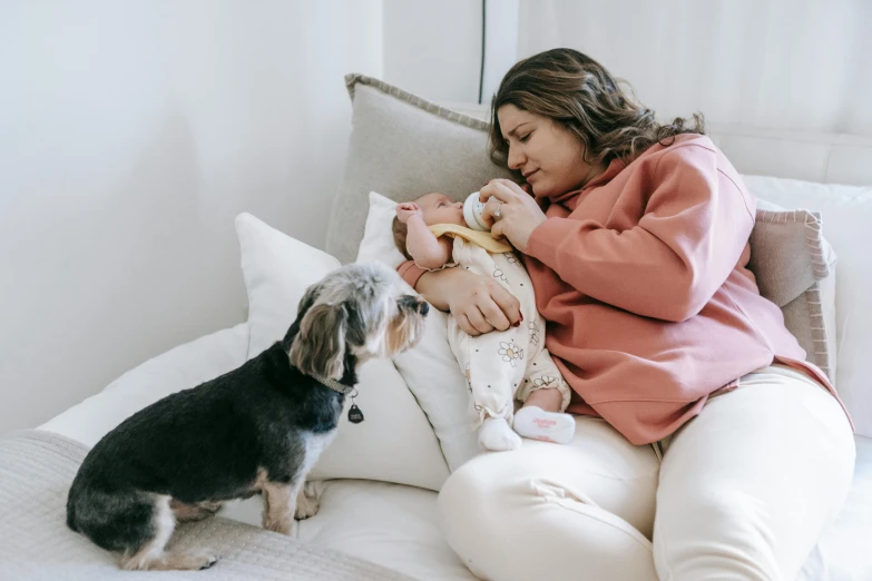 a woman sitting on top of a bed next to a dog, babies in her lap, profile image, australian, having a snack