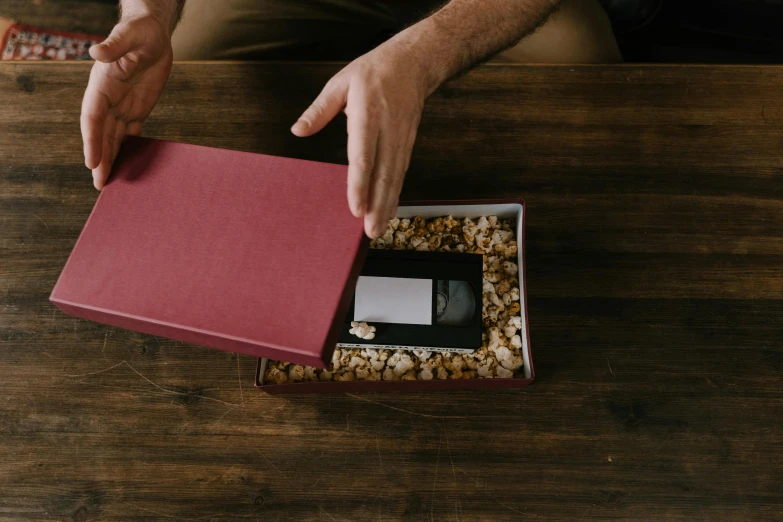 a man opening a red box on top of a wooden table, pexels contest winner, video art, packaging, home album pocket camera photo, glowforge template, vhs video