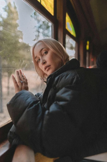 a woman sitting on a train looking out the window, a portrait, inspired by Elsa Bleda, trending on pexels, ava max, she wears a jacket, bus, promotional image