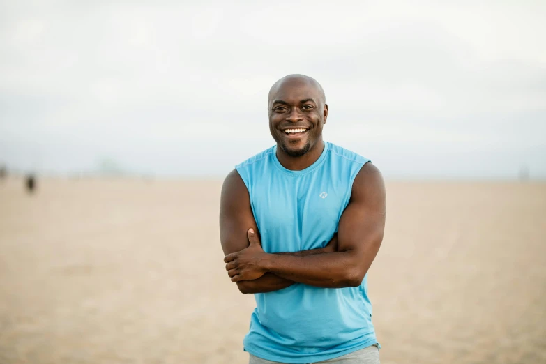 a man standing on top of a sandy beach, a portrait, by Stokely Webster, wearing fitness gear, brown skin man with a giant grin, huell babineaux, headshot profile picture