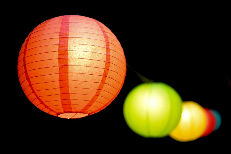 a bunch of paper lanterns hanging from a string, pexels, light and space, vibrant red and green colours, two moons lighting, with a black background, orange