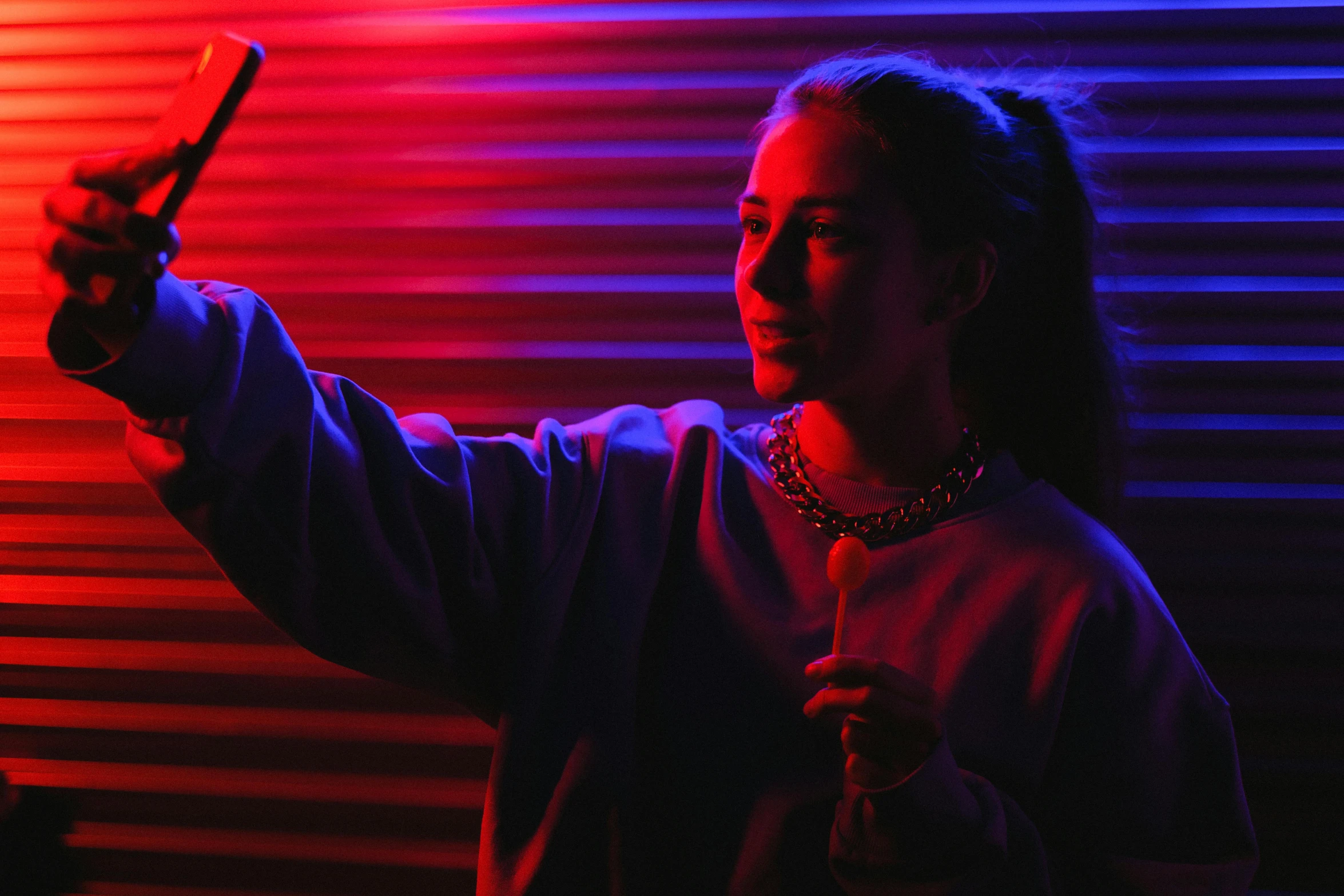 a woman holding a cell phone up to her ear, a picture, inspired by Elsa Bleda, pexels contest winner, red and blue neon, taking a selfie, holding a red lightsaber, teenage girl