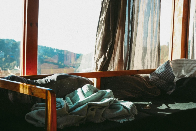 a bed with a blanket on top of it next to a window, inspired by Elsa Bleda, trending on unsplash, visual art, sitting alone in a cafe, in the sun, old couch, sol retreat