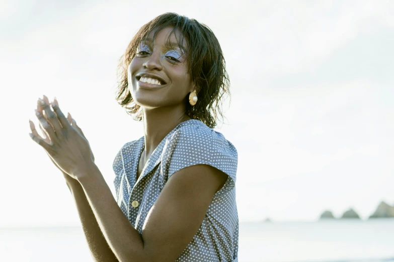 a woman standing on top of a beach next to the ocean, an album cover, pexels contest winner, brown skin man with a giant grin, photo of a hand jewellery model, relaxed. blue background, willow smith young