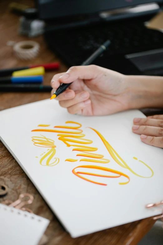 a close up of a person writing on a piece of paper, a drawing, trending on pexels, arbeitsrat für kunst, yellow and ornage color scheme, flowing lettering, airbrush, elegant drawing