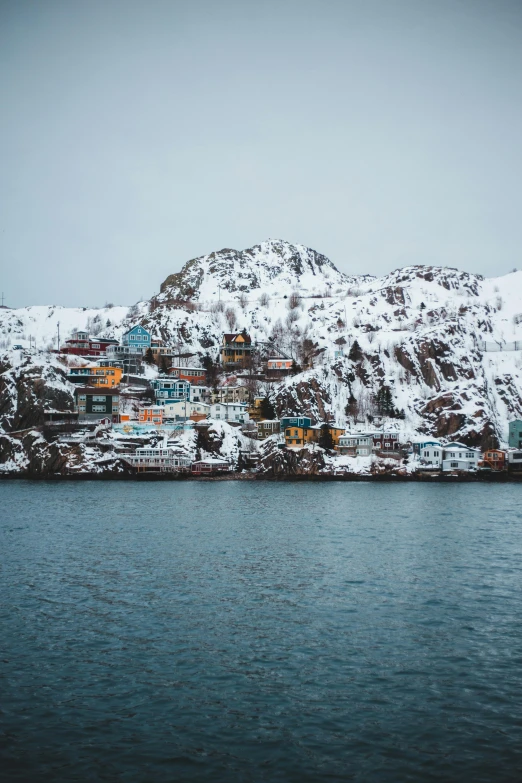 a mountain covered in snow next to a body of water, colorful houses, archipelago, muted cold colors, unsplash photography