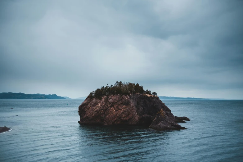 a small island in the middle of the ocean, unsplash contest winner, overcast gray skies, igneous rock, brown, tyler west