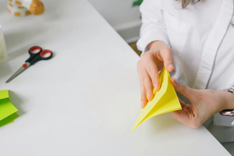 a close up of a person cutting paper on a table, yellow, prop, nursing, origami