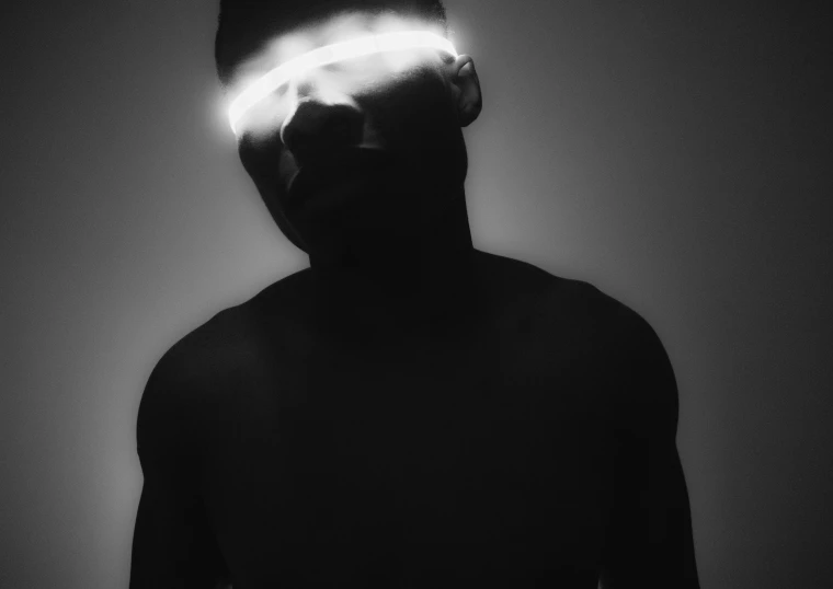 a black and white photo of a man with a light on his face, by Adam Marczyński, afrofuturism, blindfolded, childish gambino, female cyborg black silhouette, promo image