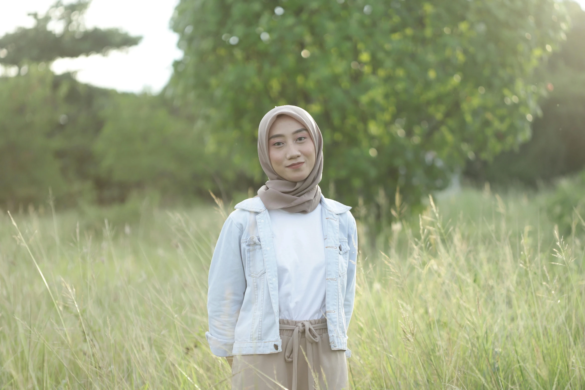 a woman standing in a field of tall grass, a picture, inspired by Kim Jeong-hui, pexels contest winner, hurufiyya, wearing casual clothes, south east asian with round face, white hijab, denim