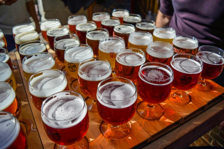 a bunch of beer glasses sitting on top of a wooden table, by Jessie Algie, pexels, crimson and white color scheme, tamborine, lots of people, on a wooden tray