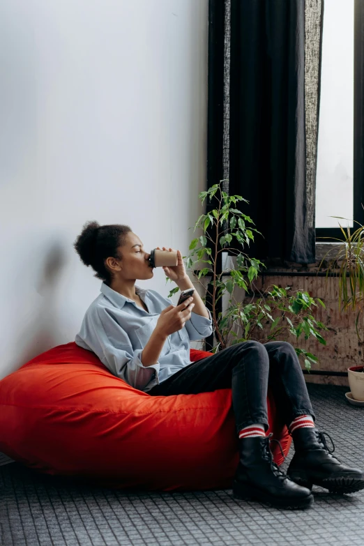 a woman sitting on a red bean bag chair, inspired by Sarah Lucas, pexels contest winner, drinking a coffee, plants, black young woman, city apartment