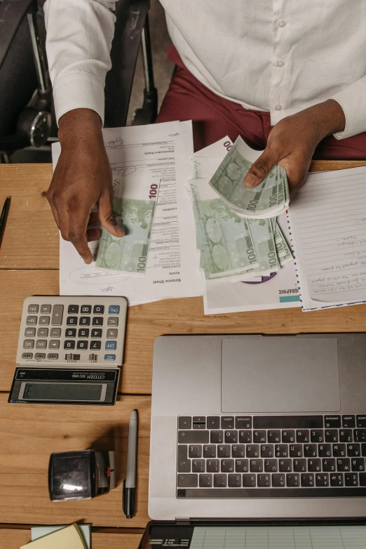 a person sitting at a desk with a laptop and a calculator, by Tobias Stimmer, pexels contest winner, renaissance, made of money, rosen zulu, settlement, high quality screenshot