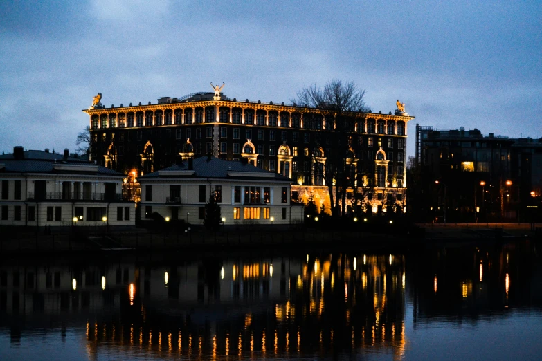 a large building sitting next to a body of water, a photo, by Serhii Vasylkivsky, neoclassicism, with glowing windows, dark building, russian style, at the waterside