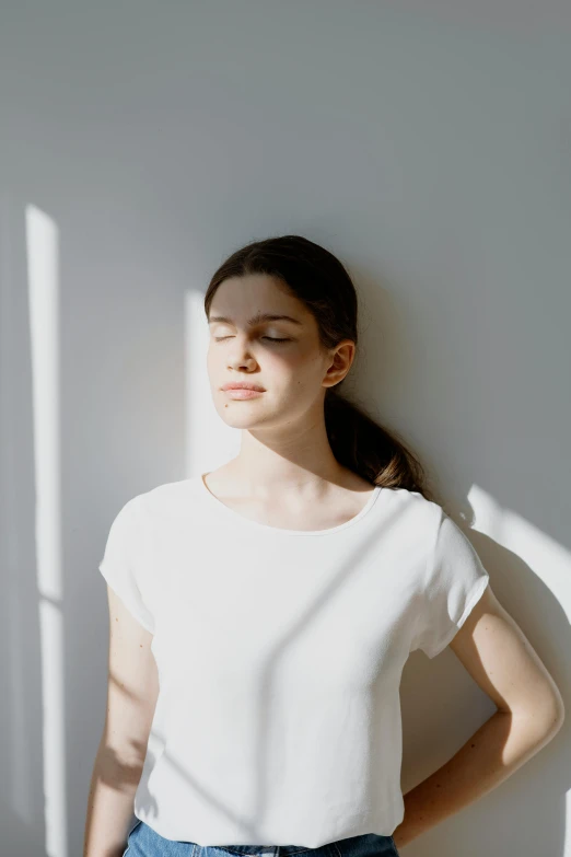 a woman leaning against a wall with her eyes closed, light and space, dressed in a white t shirt, sun overhead, in a white room, hard breathing