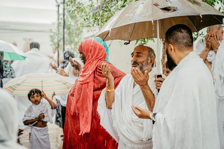 a group of people standing under umbrellas in the rain, hurufiyya, white robe with gold accents, drinking, in socotra island, connection rituals