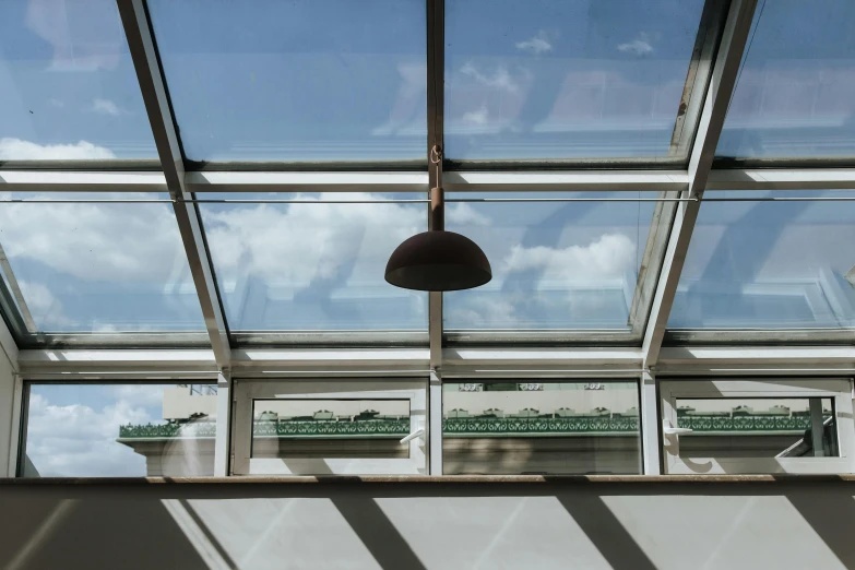 a lamp hanging from the ceiling of a building, inspired by William Nicholson, unsplash, light and space, glass greenhouse, vignette of windowsill, fully open sky, shot from roofline