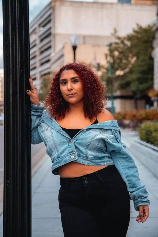 a woman leaning against a pole on a city street, trending on pexels, realism, jean jacket, full figured, wearing crop top, asher duran