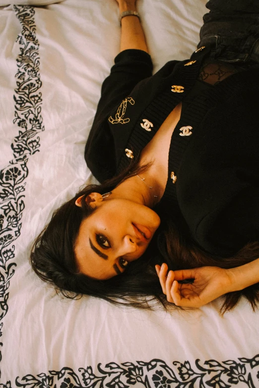 a beautiful young woman laying on top of a bed, inspired by Elsa Bleda, trending on pexels, black outfit, hindu aesthetic, cardigan, golden detailing