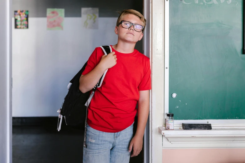 a young man standing in front of a blackboard, pexels, red t-shirt, school bag, lachlan bailey, glasses |