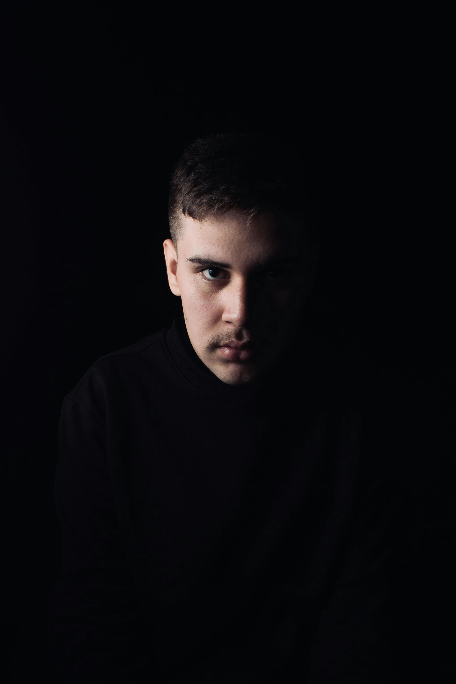 a man in a black shirt in the dark, an album cover, unsplash, realism, unibrow, serious expression, ansel ], mr beast