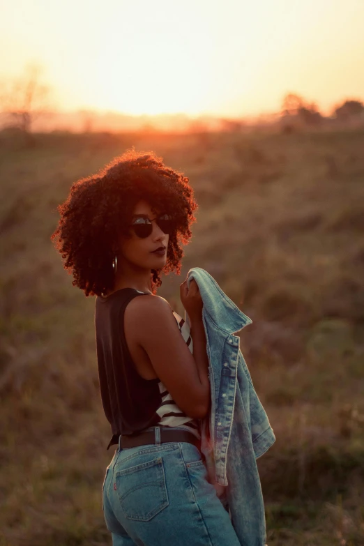 a woman standing in a field at sunset, pexels contest winner, afrofuturism, (dark shorter curly hair), with sunglasses, handsome girl, instagram photo