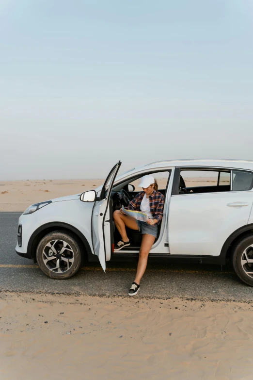 a woman sitting in the open door of a white suv, pexels contest winner, happening, in the desert beside the gulf, square, head down, car design