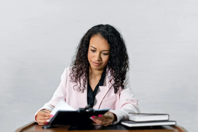 a woman sitting at a table reading a book, wearing a light - pink suit, school curriculum expert, profile image, thumbnail