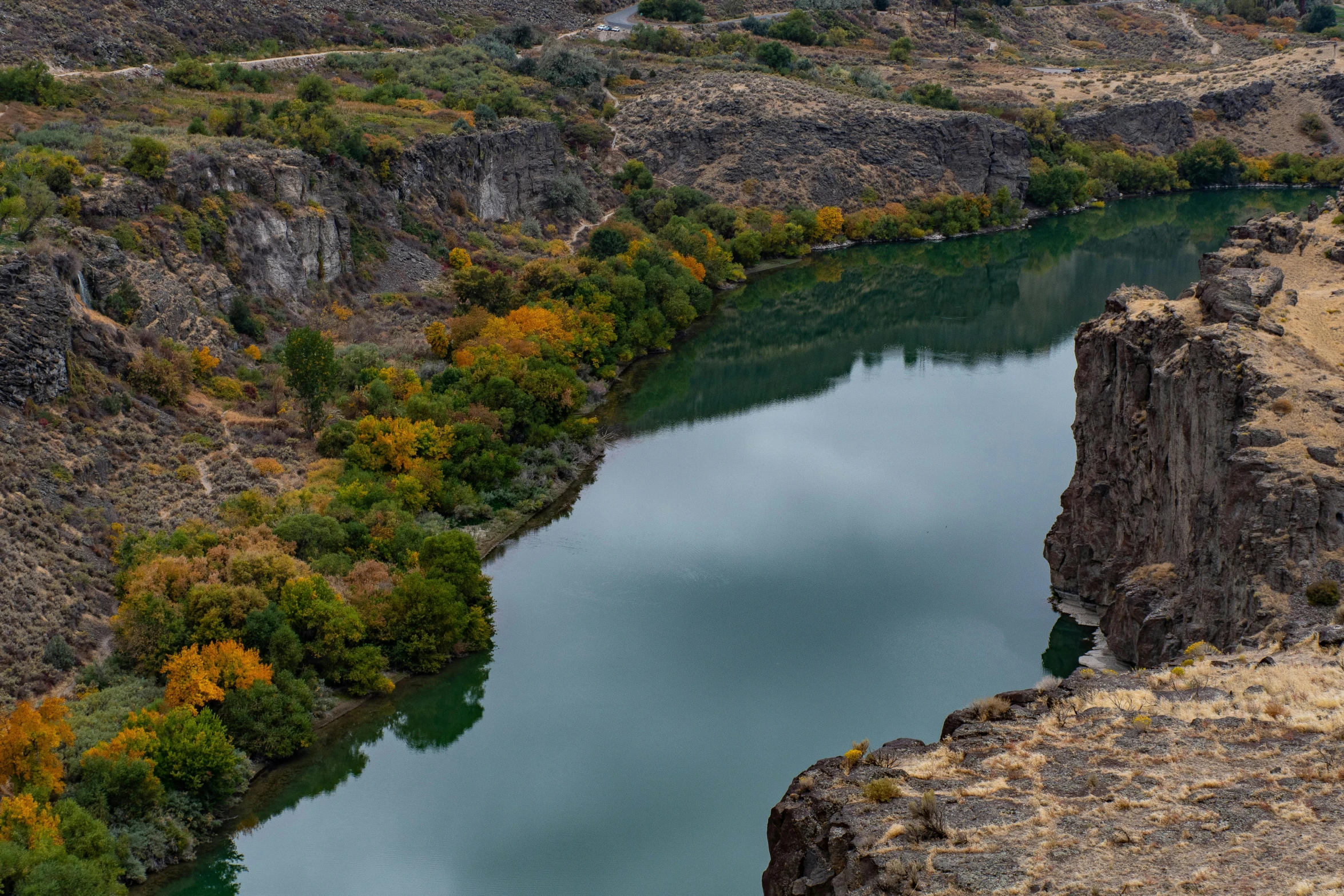 a man standing on top of a cliff next to a river, by Muggur, pexels contest winner, hurufiyya, oregon trail, mid fall, iron smelting pits, thumbnail