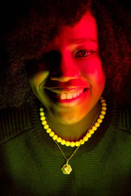 a close up of a person with a necklace on, an album cover, inspired by Carrie Mae Weems, pexels contest winner, glowing neon, happily smiling at the camera, backlight glow, nettie wakefield