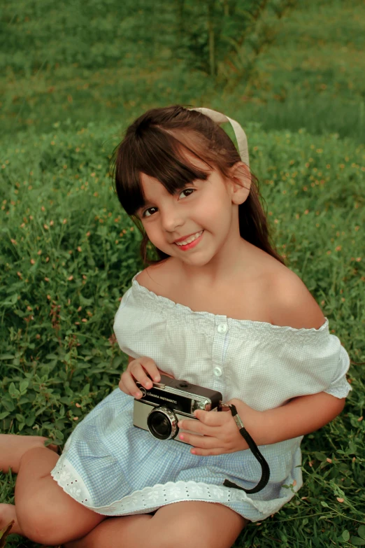 a little girl sitting in the grass holding a camera, inspired by Diane Arbus, pixabay contest winner, photorealism, 🤤 girl portrait, isabela moner, 1960s color photograph, screensaver