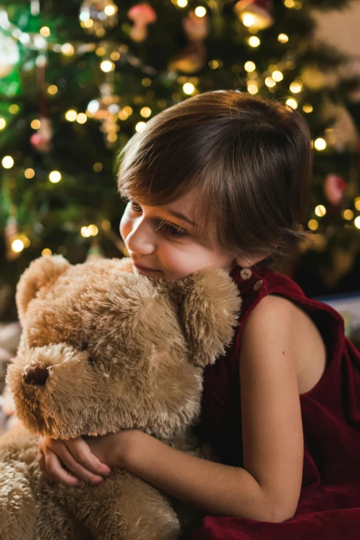 a little girl hugging a teddy bear in front of a christmas tree, a portrait, pexels, girl with dark brown hair, low detail, boys, tan