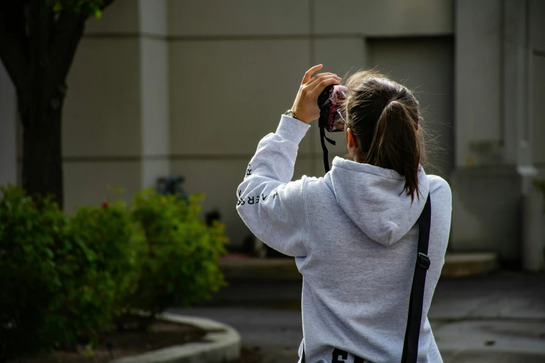a woman taking a picture with her camera, a picture, by Robbie Trevino, girl wearing hoodie, candid, student, rear-shot