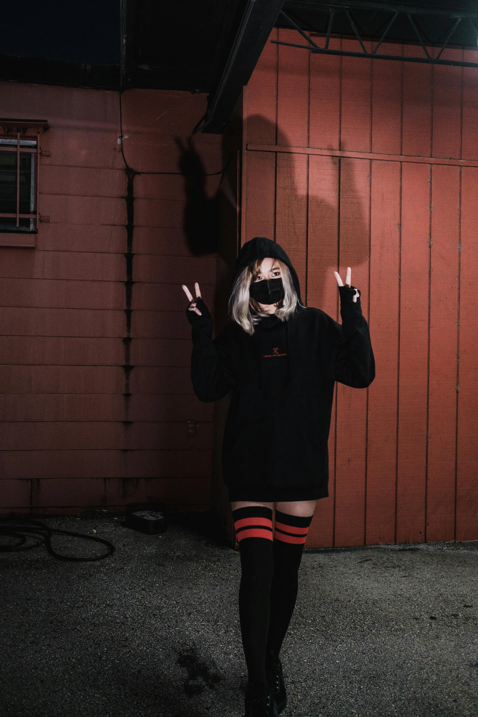 a person standing in front of a red building, inspired by Elsa Bleda, unsplash, graffiti, dressed black hoodie, thigh high socks, devil horns, shrugging