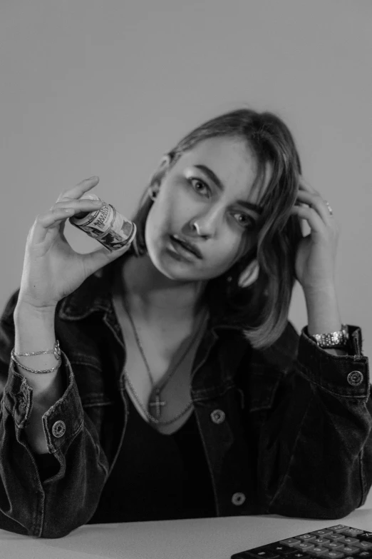 a black and white photo of a woman sitting at a table, a black and white photo, trending on pexels, photorealism, portrait sophie mudd, dressed in leather jacket, photo of a hand jewellery model, taken in the late 2000s