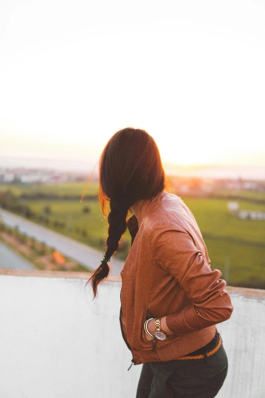 a woman riding a skateboard on top of a ramp, a picture, trending on pexels, happening, braided brown hair, looking out at a sunset, arm around her neck, brown leather jacket