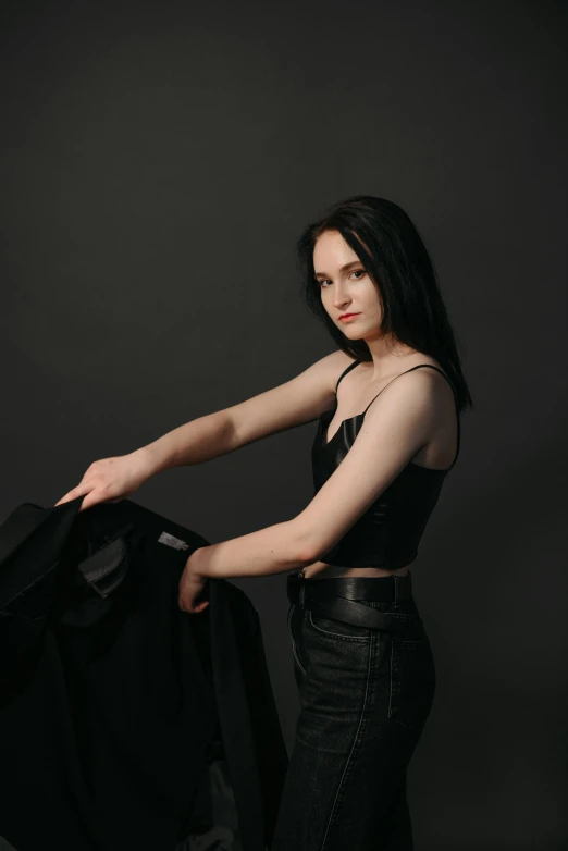 a woman in a black top is holding a jacket, a pale skin, she has black hair, shot with sony alpha, high quality image