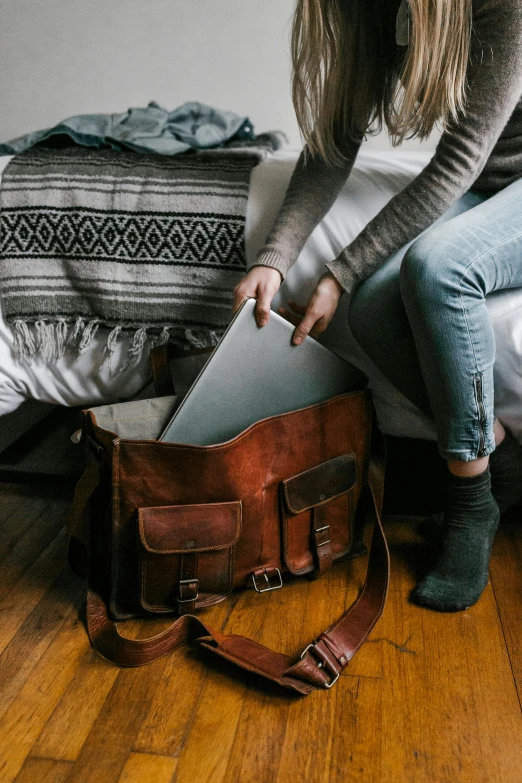 a woman sitting on a bed holding a laptop, leather pouch, well worn, adventuring, full width