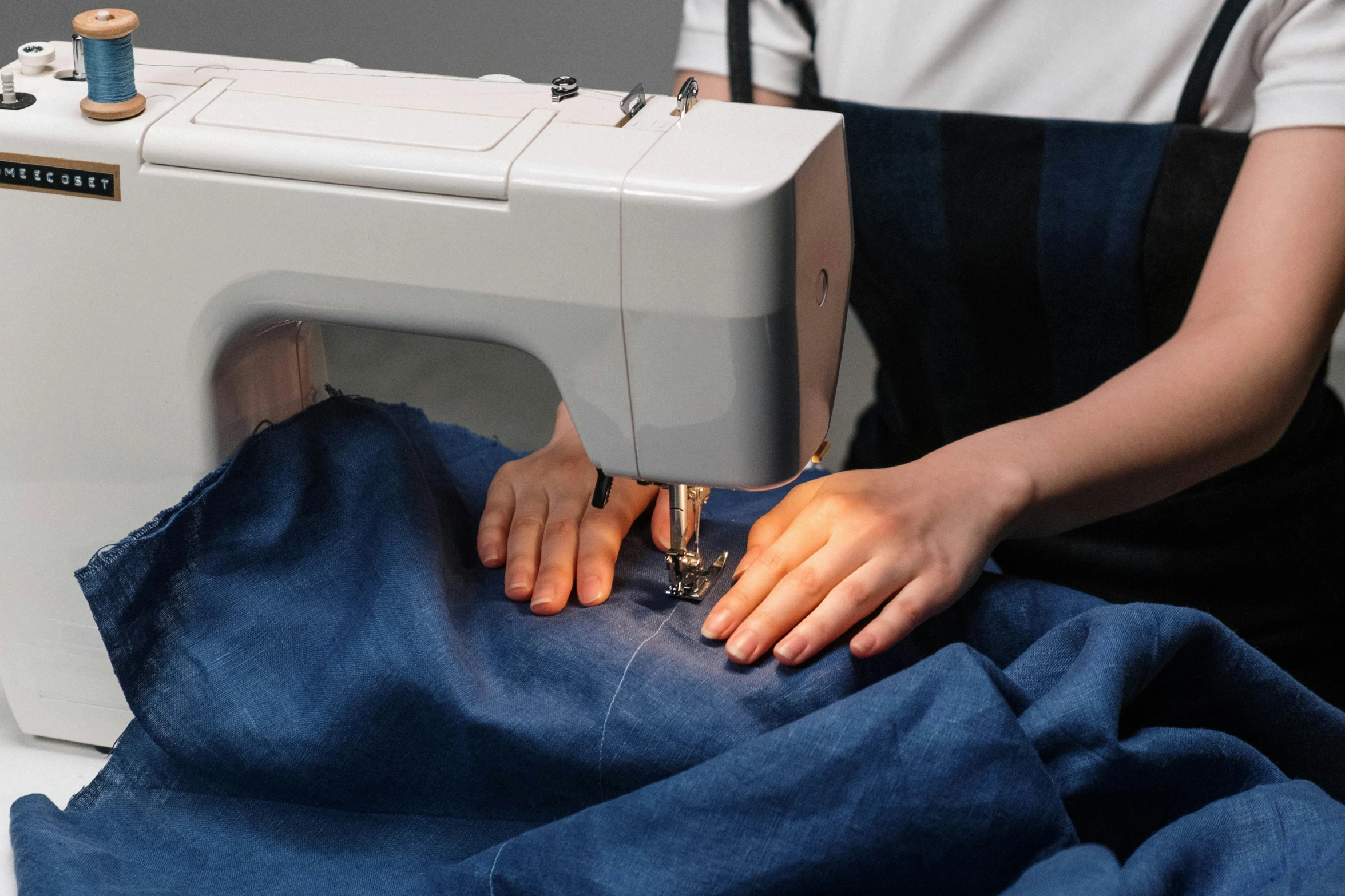 a woman is working on a sewing machine, a hyperrealistic painting, inspired by Lorenzo Lotto, unsplash, denim, navy, medium angle, nursing