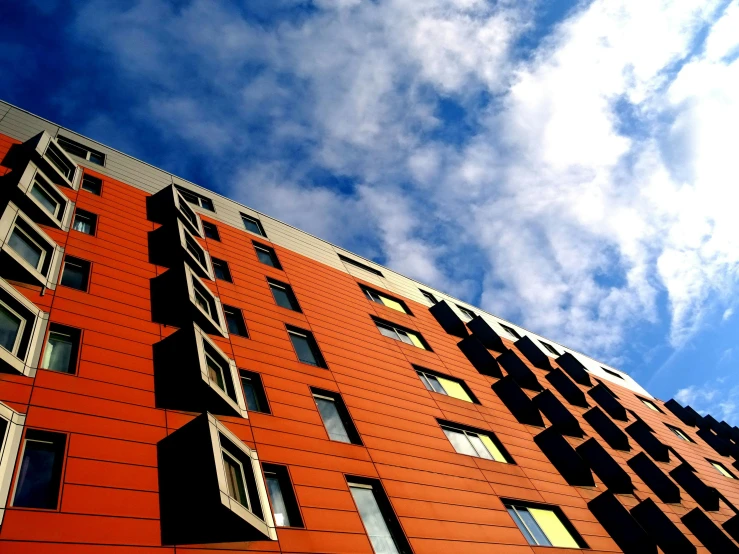 a tall red building with lots of windows, inspired by Washington Allston, unsplash, bauhaus, black and orange, orange clouds, contrasting colours, looking upwards