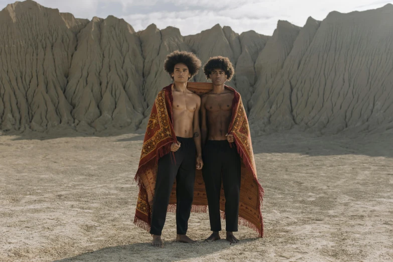 two people standing next to each other in the desert, an album cover, unsplash, renaissance, wearing cave man clothes, 14 yo berber boy, [ theatrical ], with afro