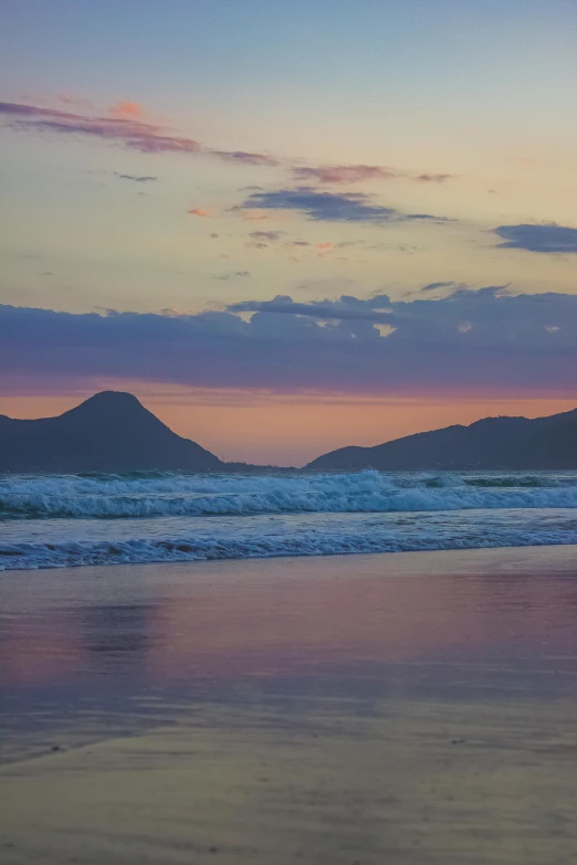 a man riding a surfboard on top of a sandy beach, during a sunset, mountains and oceans, purple hues, rio de janeiro