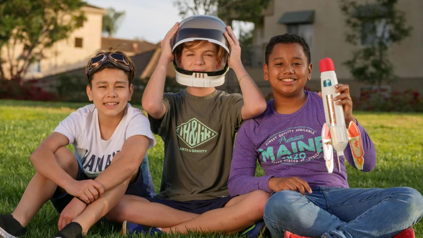 a group of kids sitting on top of a lush green field, a portrait, by Wayne England, pexels contest winner, holding a rocket, full product shot, 3 heads, mars vacation photo