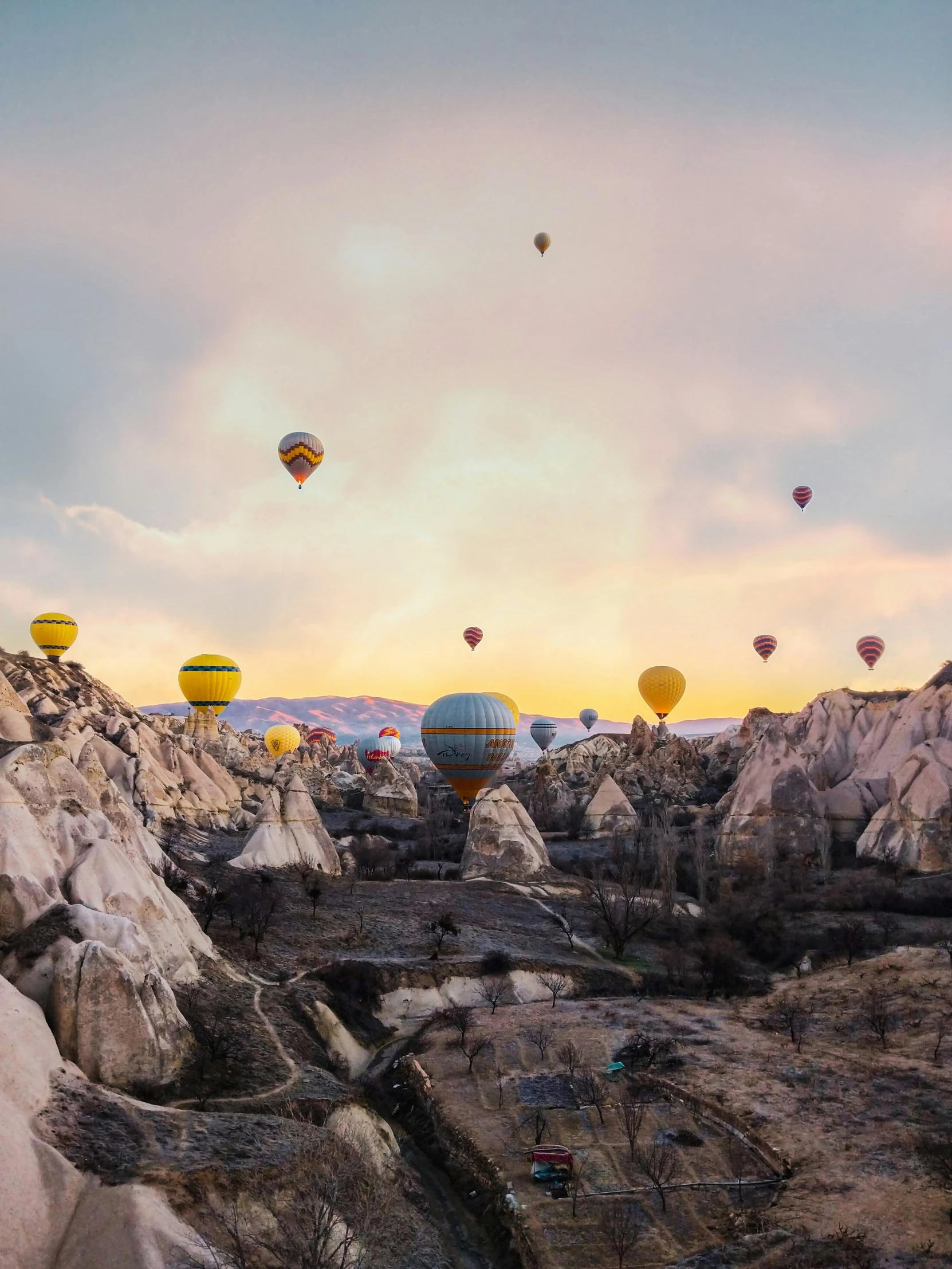 a group of hot air balloons flying over a rocky landscape, by irakli nadar, pexels contest winner, 4 k cinematic panoramic view, a quaint, cozy, cinematic”